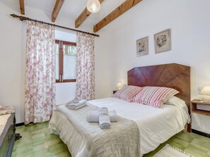 A bedroom with a bed, curtains, a headboard, a nightstand, and a wall with two framed pictures.