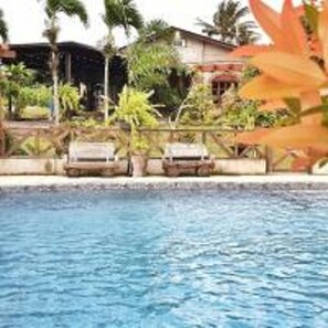 Una piscina con sillones de descanso y palmeras al fondo.
