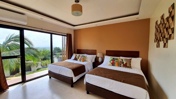 Habitación de hotel con dos camas, un gran ventanal corredero que da a un balcón y vistas a palmeras.
