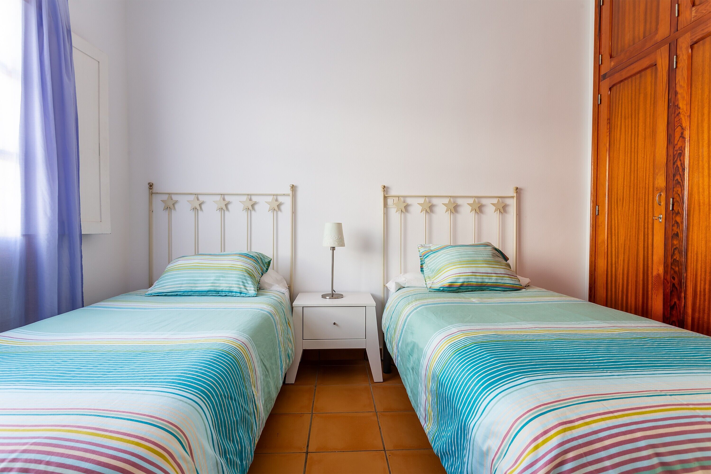 Une chambre avec deux lits, une table de chevet avec une lampe et une armoire en bois.