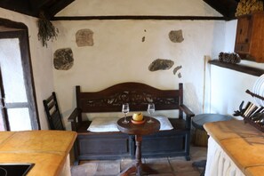Ein rustikaler Raum mit einer Holzbank, einem kleinen Tisch mit Schüssel und Gläsern sowie einer Steinwand mit Farbflecken.