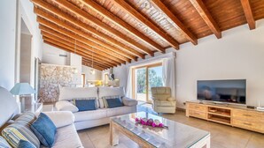 A living room with a sofa, coffee table, TV, and wooden ceiling beams.