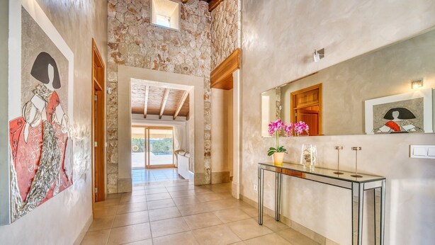 A hallway with a stone wall, a glass console table with a vase of flowers, and a framed artwork on the wall.
