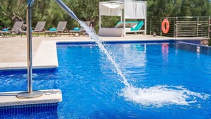A swimming pool with a water spout, lounge chairs, and a canopy structure.