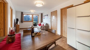 A modern kitchen with wooden cabinets, a dining table with a red table runner, and a view of mountains through the window. - Rustic Apartment Vermoi on Mountain Farm with Terrace (Kastelbell-Tschars)