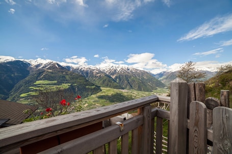 A wooden deck with a view of snow-capped mountains and green valleys.. Rustic Apartment Vermoi on Mountain Farm with Terrace