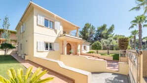 Une maison à deux étages dotée d’un balcon, d’une allée pavée et d’un jardin bien entretenu avec des palmiers.