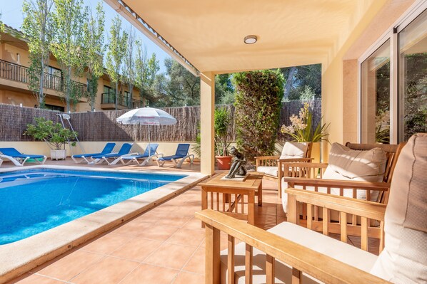A poolside area with lounge chairs, a table, and a covered seating area.