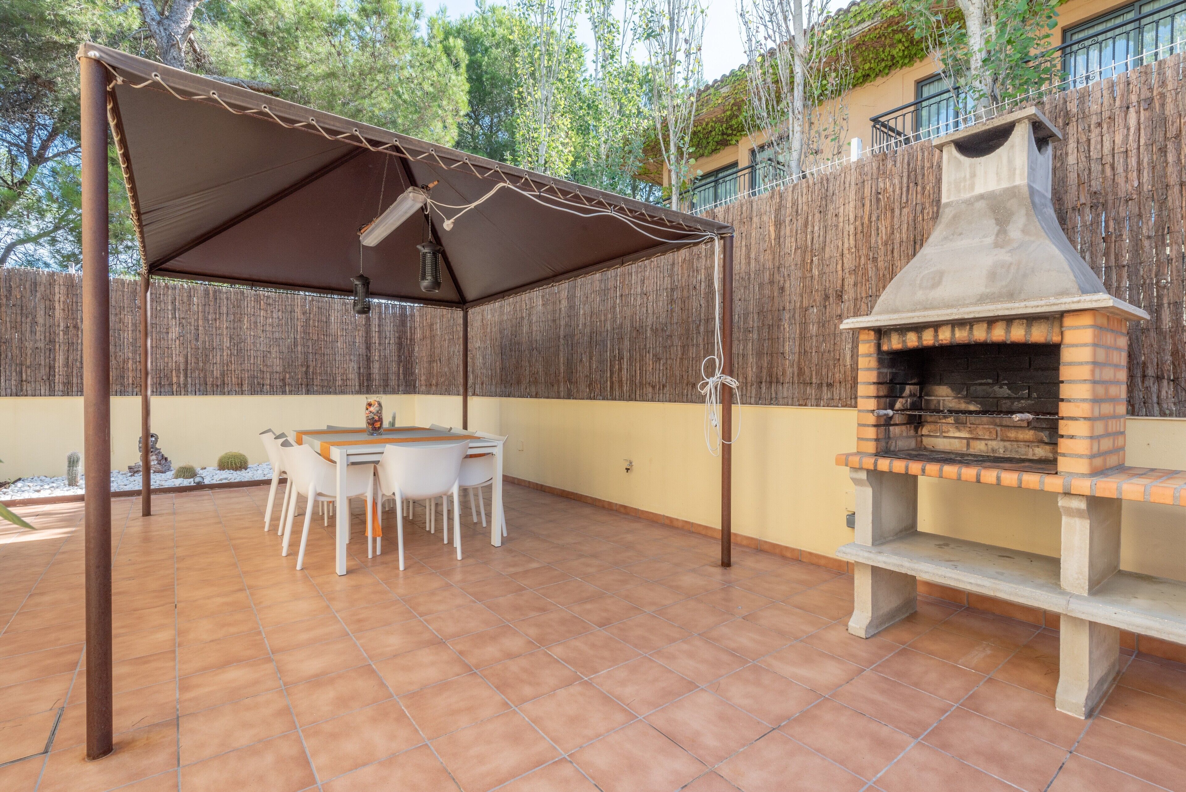 An outdoor patio with a brick oven, a covered table, and chairs.