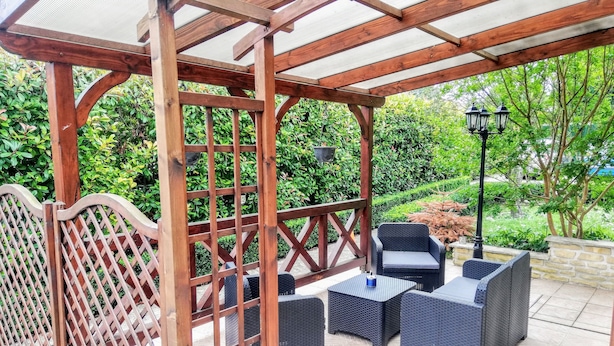 A covered outdoor seating area with wicker furniture and a wooden lattice fence.