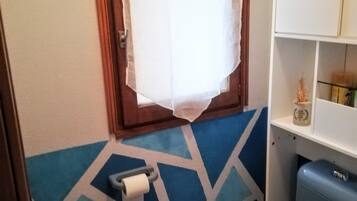 Een badkamer met een toilet, toiletpapier, een kast en een raam met gordijn.