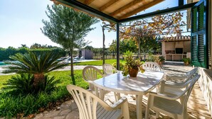 An outdoor patio with a table and chairs, surrounded by greenery and a view of a building. - Rural villa with pool – Villa Tabo (Selva)
