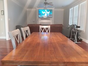 Een eetkamer met een houten tafel, witte stoelen, een televisietoestel op een meubelstuk en een plafondventilator.