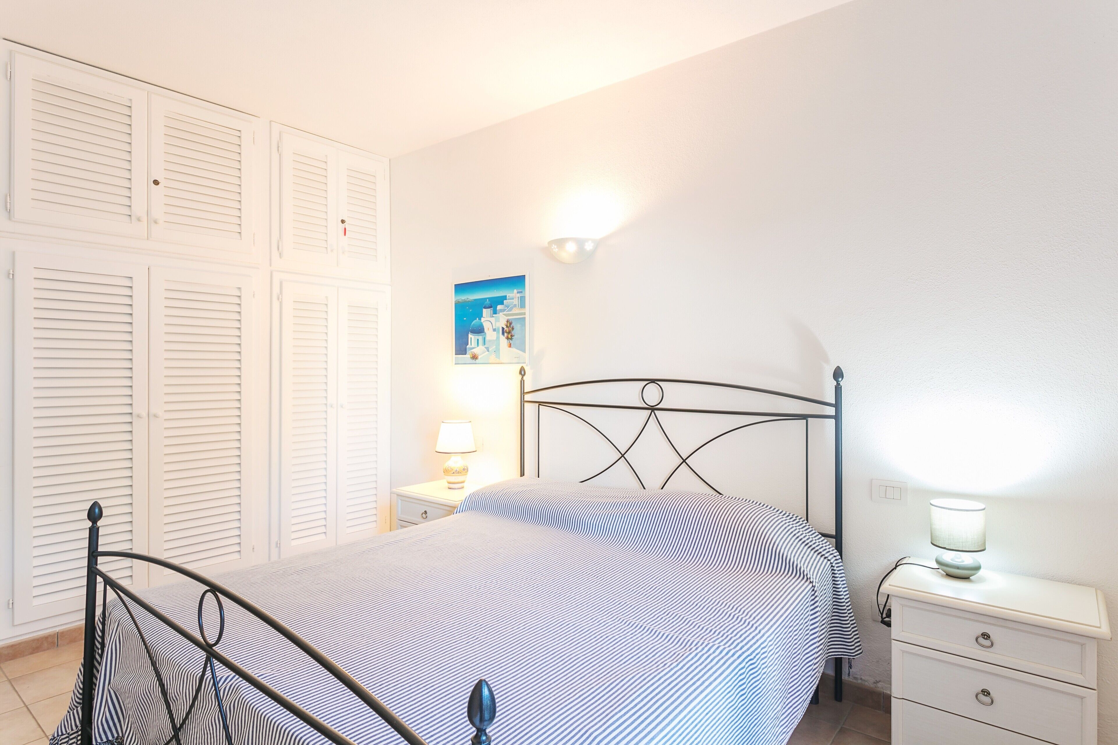 Een slaapkamer met een bed, nachtkastje, lamp, wandplank en een schilderij.