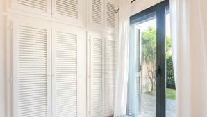 Quarto com uma janela grande, persianas brancas e edredom listrado.