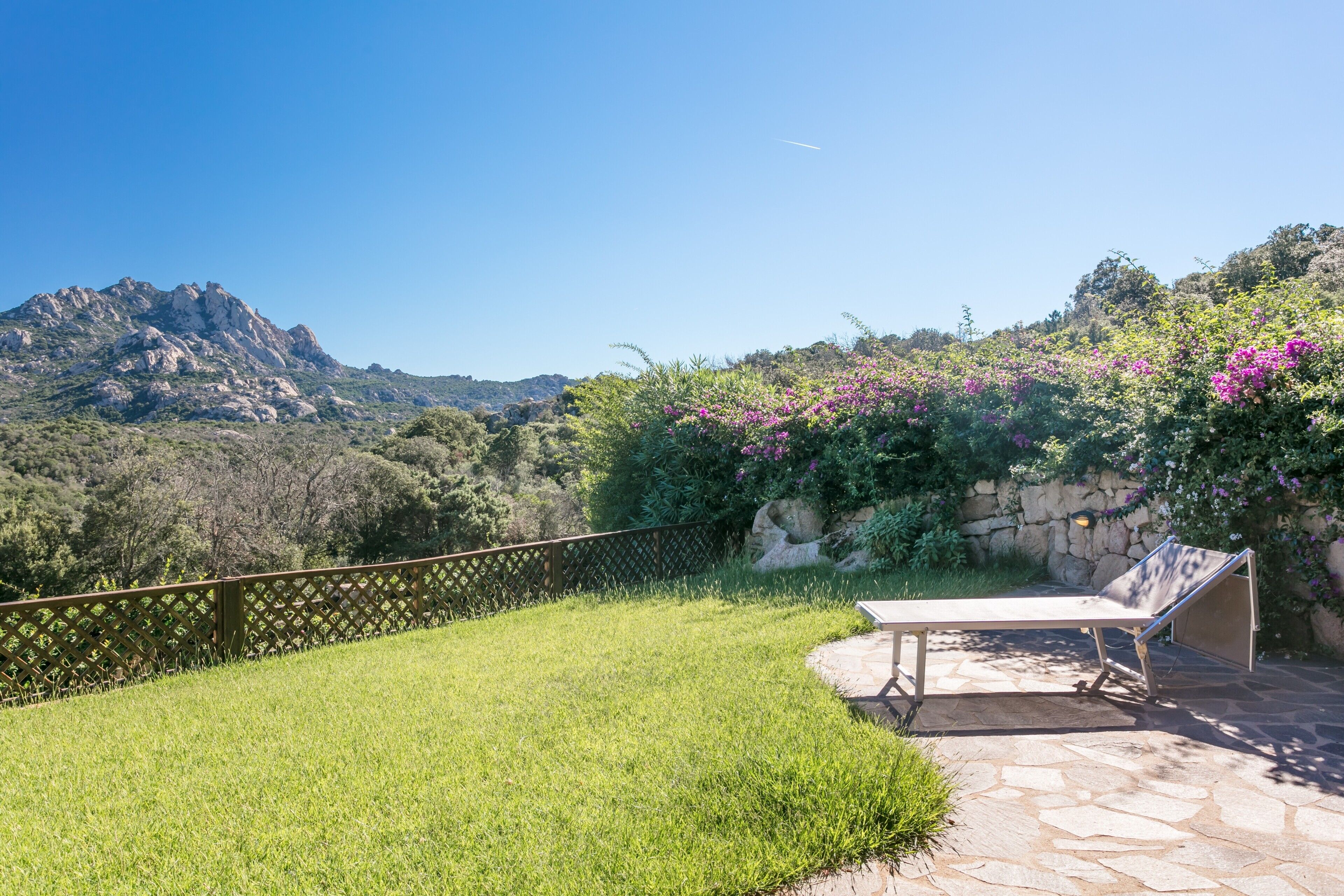 Una terrazza con tavolo e sedie, pavimento in pietra e vista su una montagna e vegetazione.