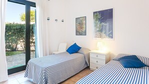 Quarto com duas camas, mesa de cabeceira, cadeira e janela com cortinas.