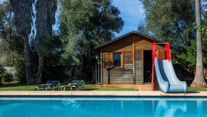 Uma cabana de madeira com um escorrega, uma piscina e duas espreguiçadeiras.