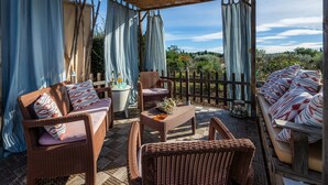 Um pátio externo com móveis de vime, uma mesa e vista para a paisagem.
