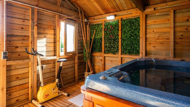 Interior de uma cabana de madeira com sauna, equipamentos de ginástica e uma janela com vista para o verde.