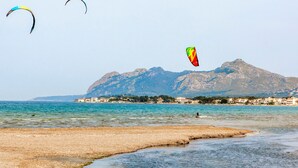 Uma praia com águas cristalinas, uma montanha ao fundo e pipas no céu.