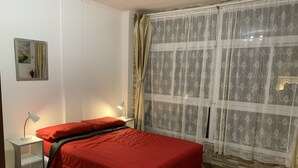 Een slaapkamer met een bed, twee bedlampen, een nachtkastje, een raam met dunne gordijnen en een schilderij aan de muur.