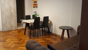 Een moderne woonkamer met een visgraatparketvloer, een grijze bank, een eettafel met stoelen en een klein bijzettafeltje.