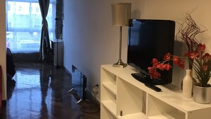 Een woonkamer met een televisie, een lamp en een plant in een pot.