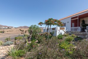 A white building with a red roof, surrounded by a garden with various plants and flowers.