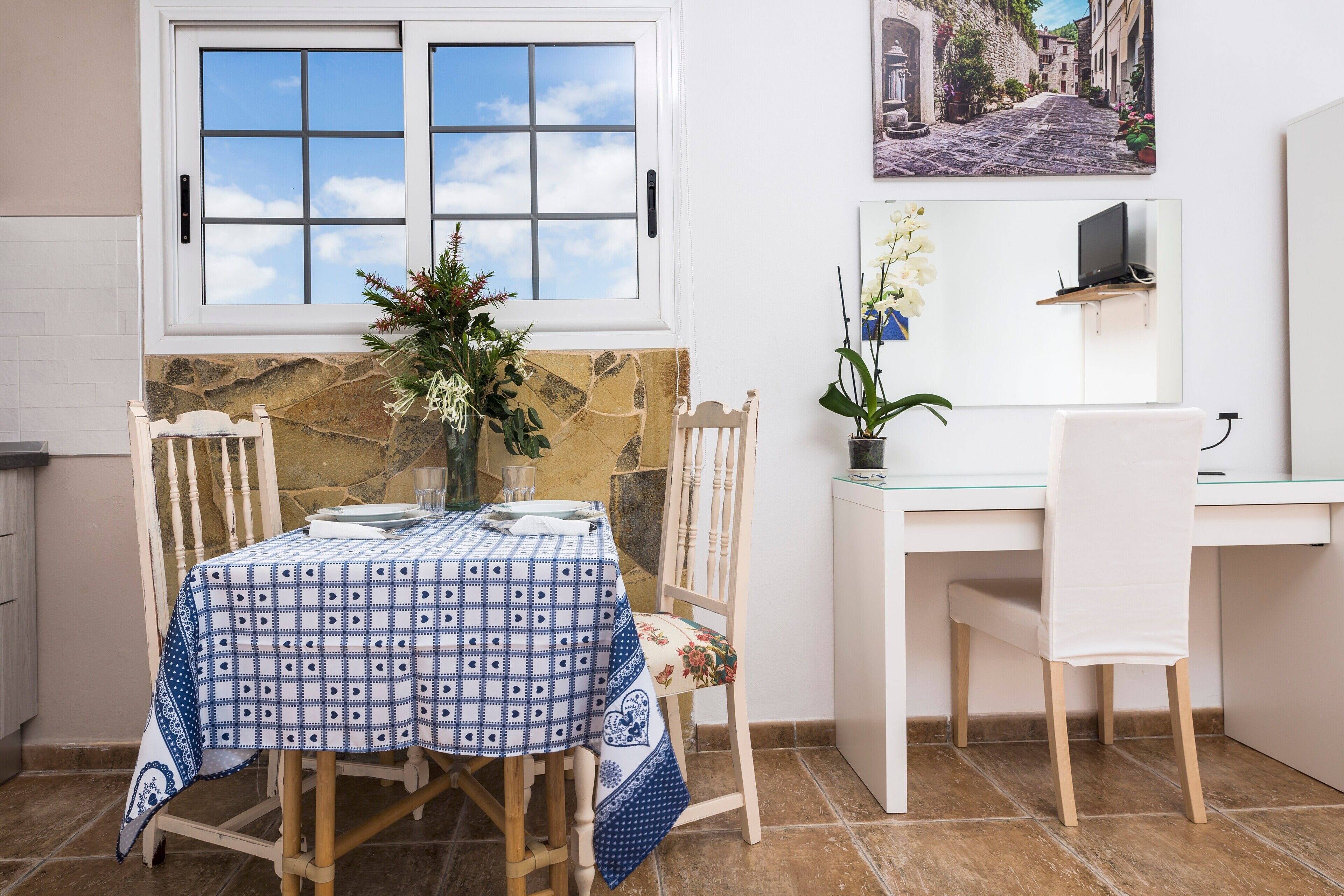 Un comedor con una mesa dispuesta para dos, una silla, una planta pequeña y una ventana con vistas a la calle.