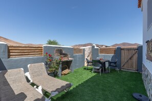 A rooftop patio with two lounge chairs, a table, and a grill.