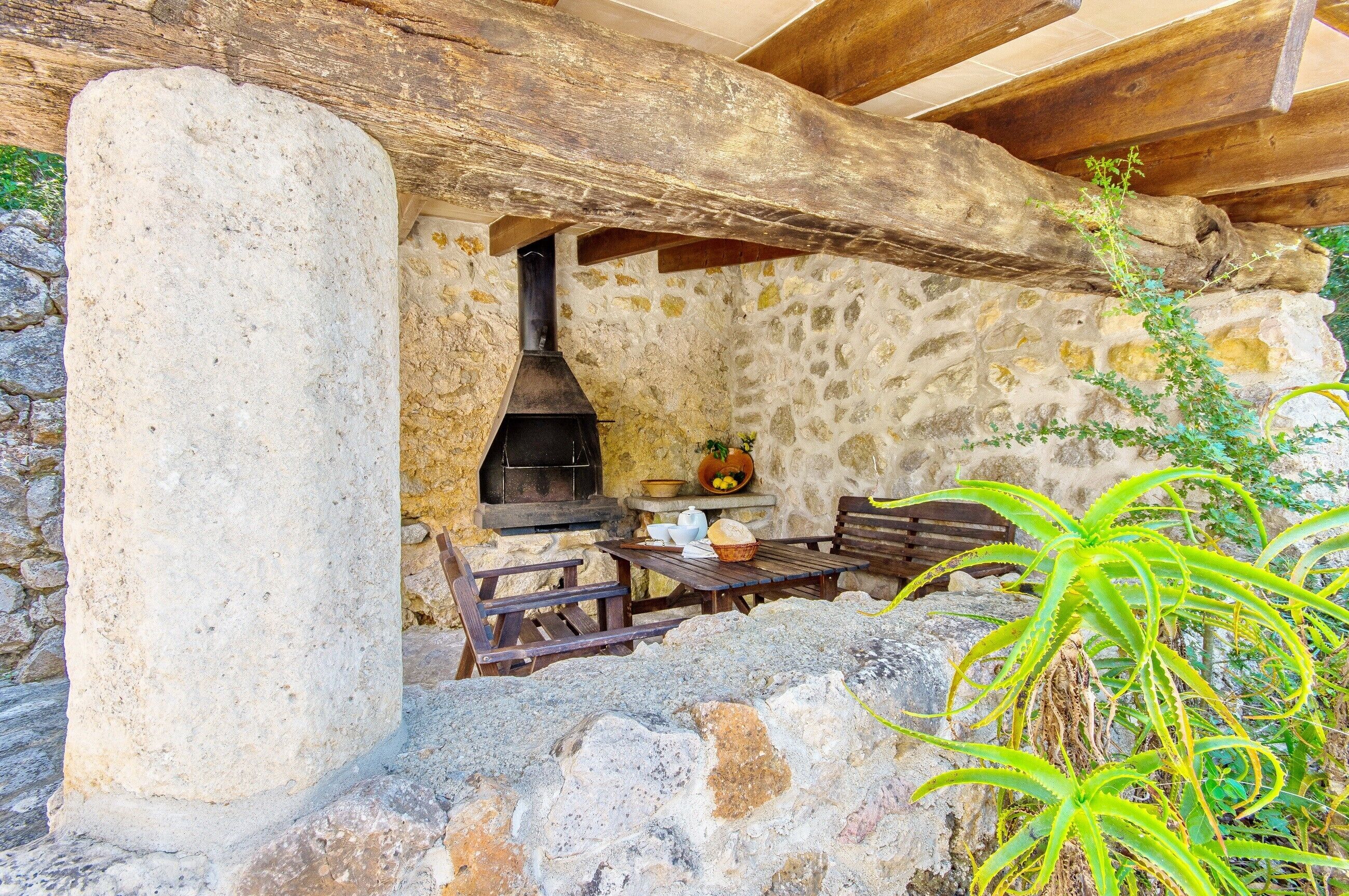 Un espacio al aire libre con paredes de piedra, una estufa de leña, un pilar de piedra y mobiliario de madera.