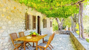 A stone wall with wooden shutters, a table with chairs, and a potted plant.