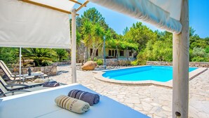 A poolside area with lounge chairs, a covered seating area, and a stone pathway leading to a pool.