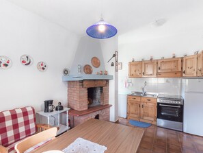 A kitchen with a brick fireplace, wooden cabinets, a stainless steel refrigerator, and a dining area with a checkered sofa.