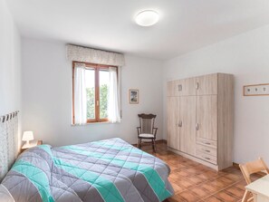 A bedroom with a bed, a chair, a wardrobe, a window, and a bedside table.