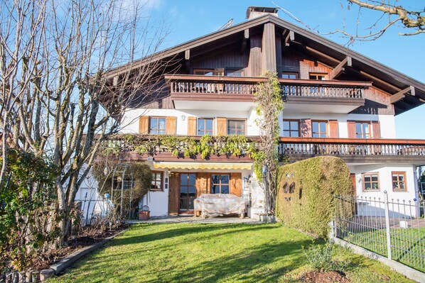A two-story wooden house with a balcony, a covered porch, and a well-maintained lawn.
