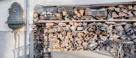 A metal bench with a checkered pattern, a metal railing, and a stack of firewood against a wall.