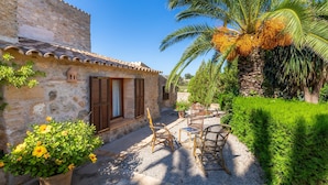 A stone building with a tiled roof, a palm tree, and outdoor furniture.