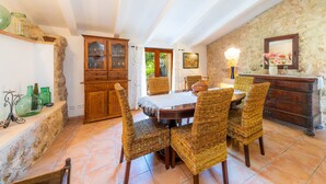 A dining area with a round table, wicker chairs, a wooden cabinet, and a stone wall.