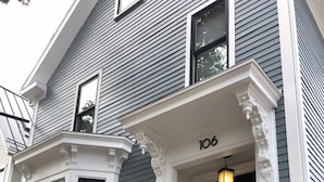 A house with a black front door, white trim, and a number '106' above the door. There are two flower pots on the steps.
