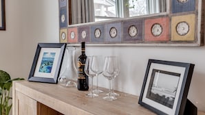 A wooden console table with a wine bottle, glasses, and framed pictures.