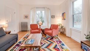 A living room with a gray sofa, two pink armchairs, a wooden coffee table, and a colorful rug.