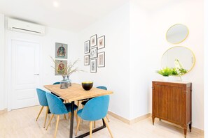A dining area with a wooden table, blue chairs, and framed artwork on the wall.
