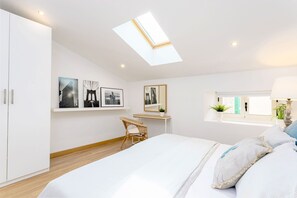 A bedroom with a skylight, a bed, a desk, and a chair.
