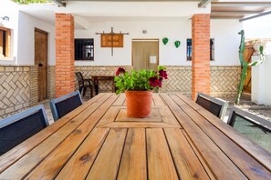 Une table en bois avec des chaises, une plante en pot et un mur en briques.