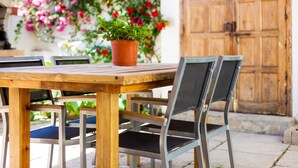 Une table en bois avec des chaises, une plante en pot et une porte en bois à l’arrière-plan.
