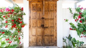 Une porte à deux battants en bois, dotée d’un loquet métallique, et encadrée de plantes vertes et de fleurs rouges.