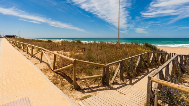 Une promenade en bois menant à une plage, avec un ciel dégagé.