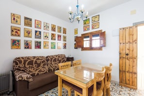 Un coin repas comprenant une table à plateau en verre, des chaises en bois, un canapé à motifs et un mur décoré de vieilles affiches.